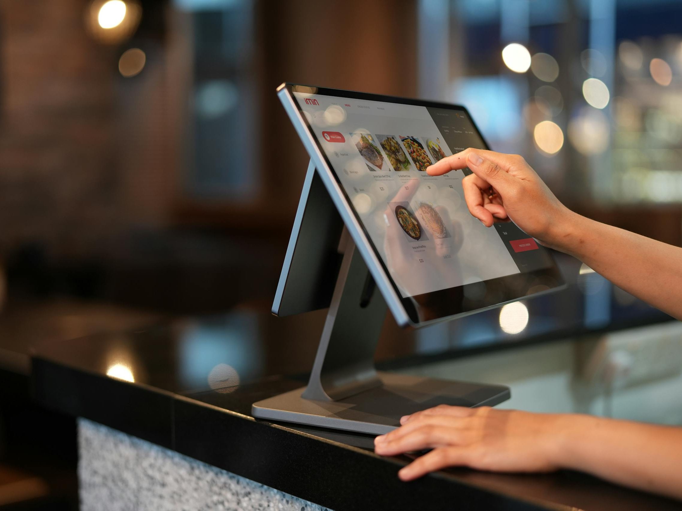Close-up of a hand interacting with a touchscreen POS system in a restaurant setting.
