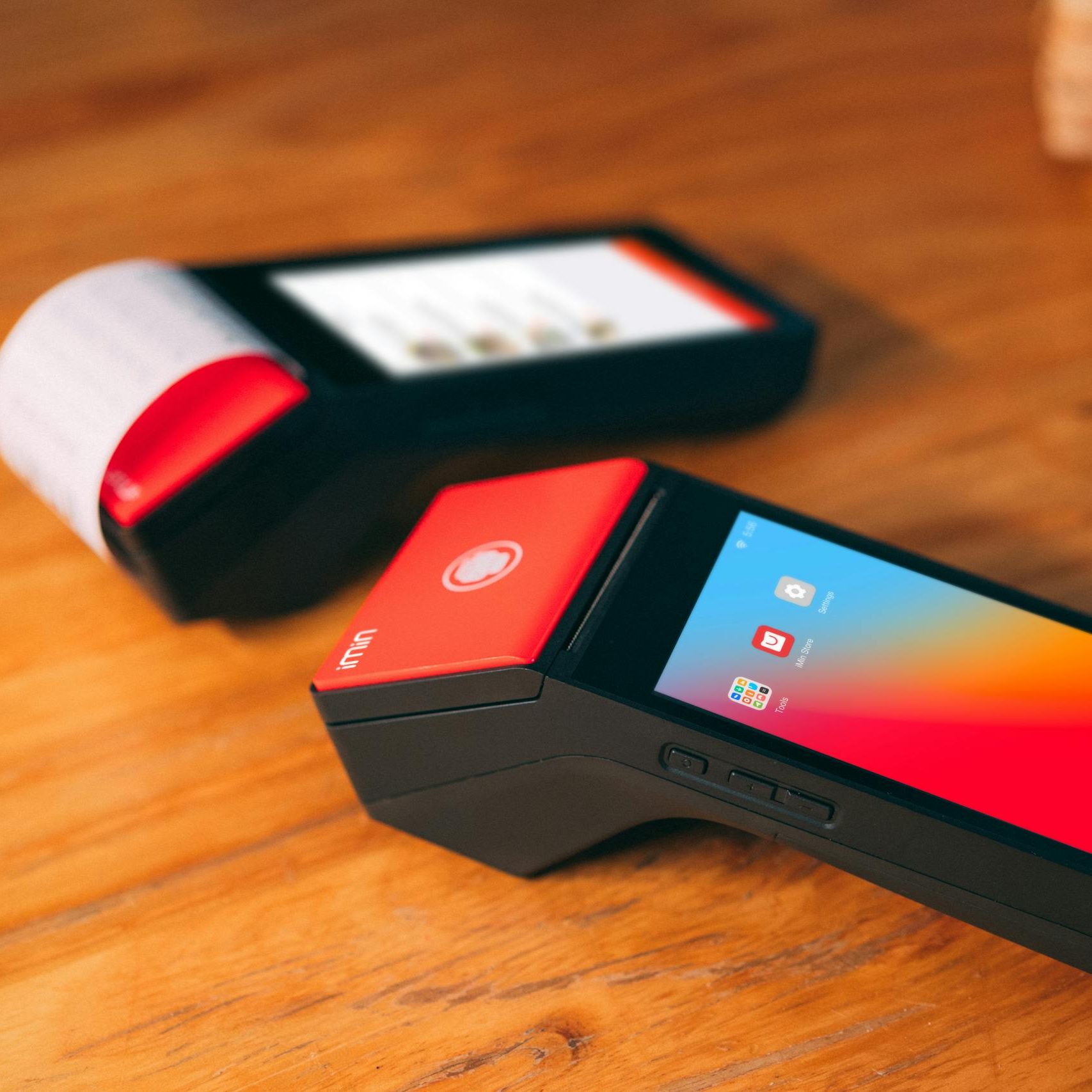 Close-up of two modern cashless payment terminals on a wooden surface, showcasing digital technology.