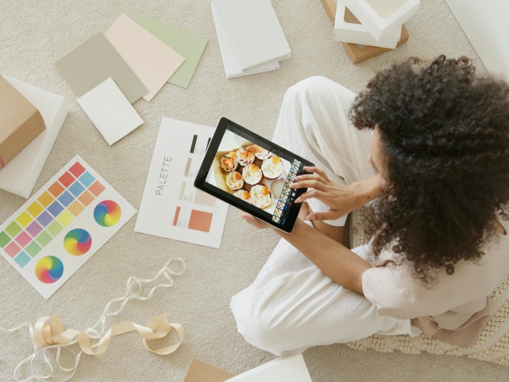 Woman using tablet surrounded by design tools and gift box, showcasing creativity and online work.